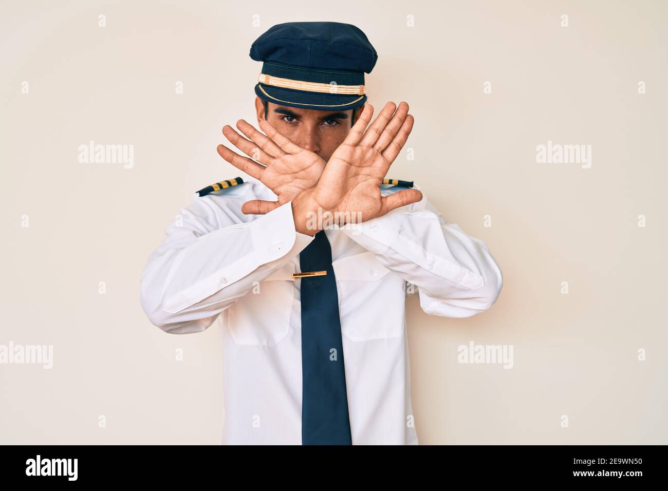 Young hispanic man wearing airplane pilot uniform rejection expression ...