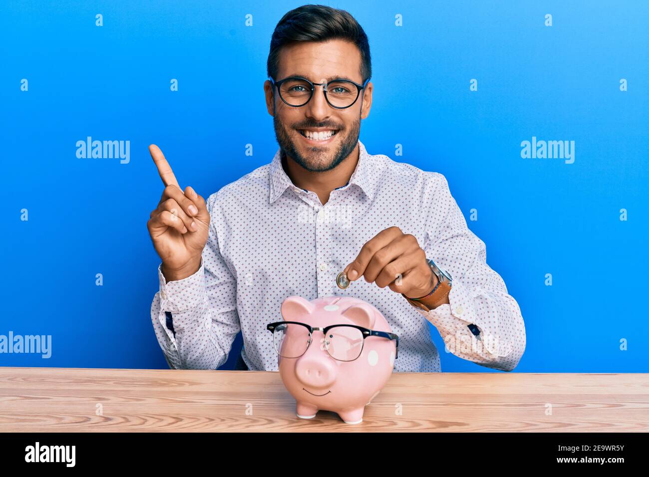 Handsome hispanic man holding piggy bank with glasses smiling happy ...