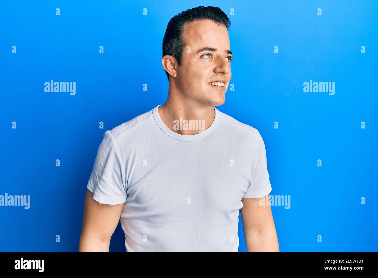 Handsome young man wearing casual white t shirt looking to side, relax ...