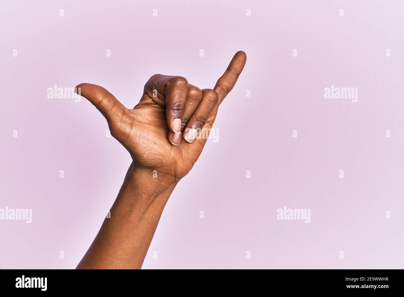 Arm and hand of black middle age woman over pink isolated background gesturing hawaiian shaka greeting gesture, telephone and communication symbol Stock Photo