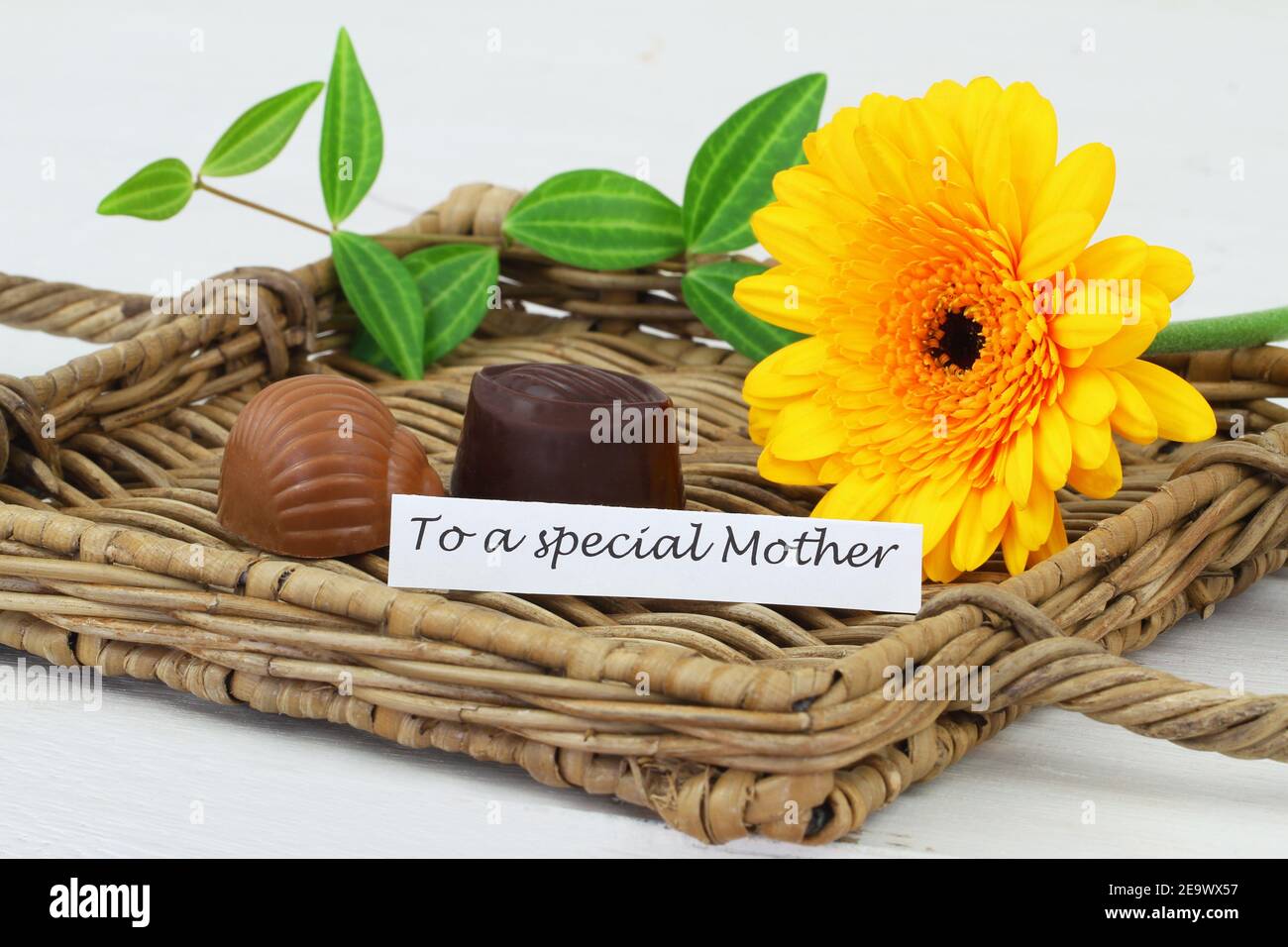 Happy Mother's day card with yellow gerbera daisy and two delicious chocolates on wicker tray Stock Photo