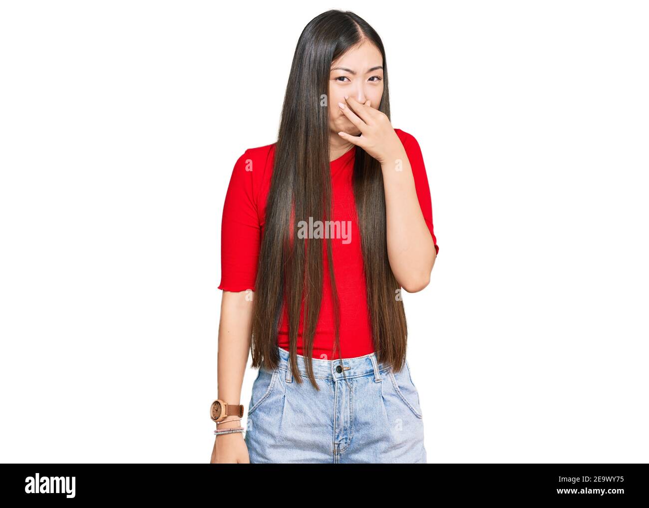 Young chinese woman wearing casual clothes smelling something stinky and disgusting, intolerable smell, holding breath with fingers on nose. bad smell Stock Photo