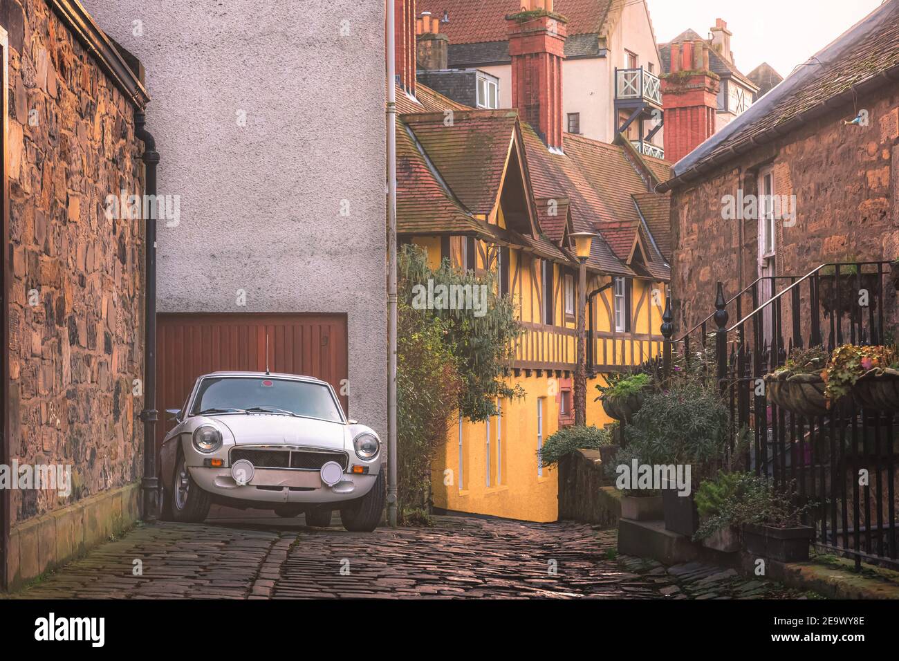 A classic vintage white sports car parked on a cobblestone lane in old