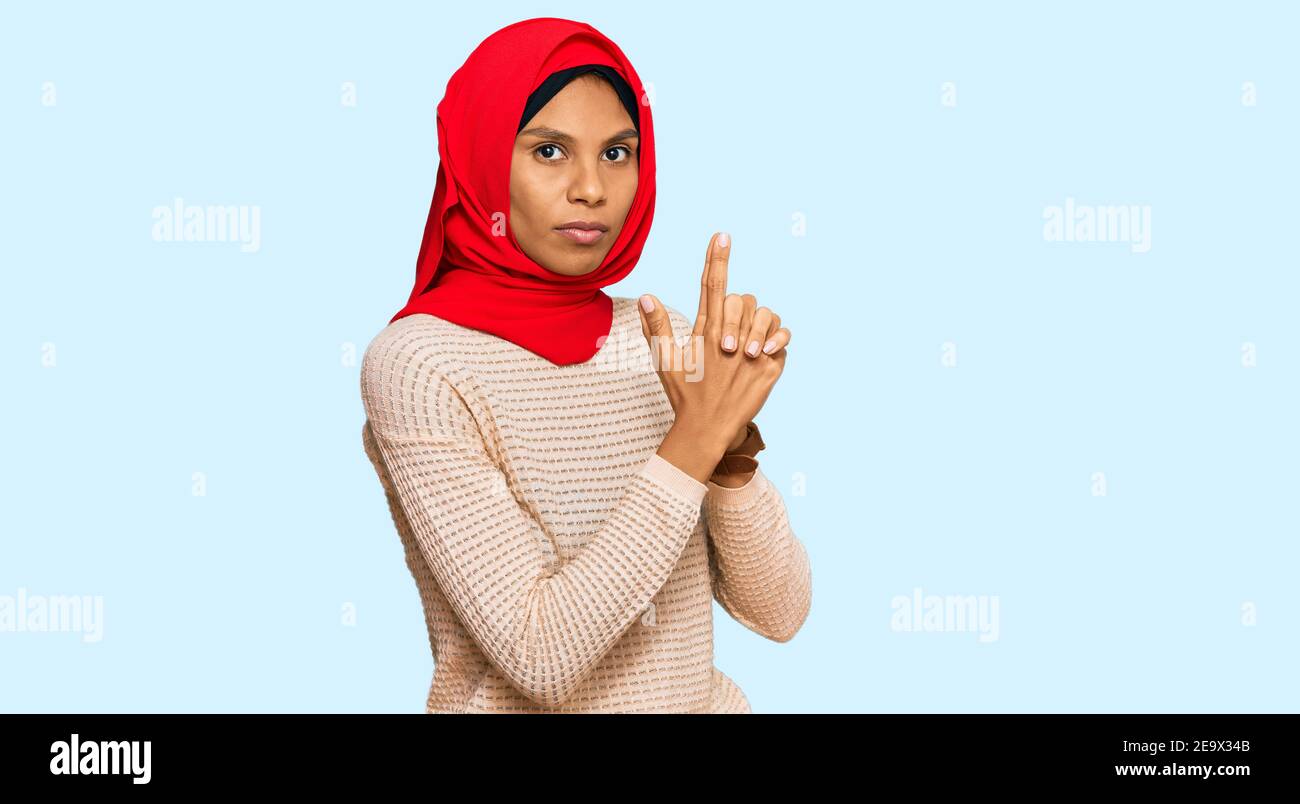 Young african american woman wearing traditional islamic hijab scarf holding symbolic gun with hand gesture, playing killing shooting weapons, angry f Stock Photo