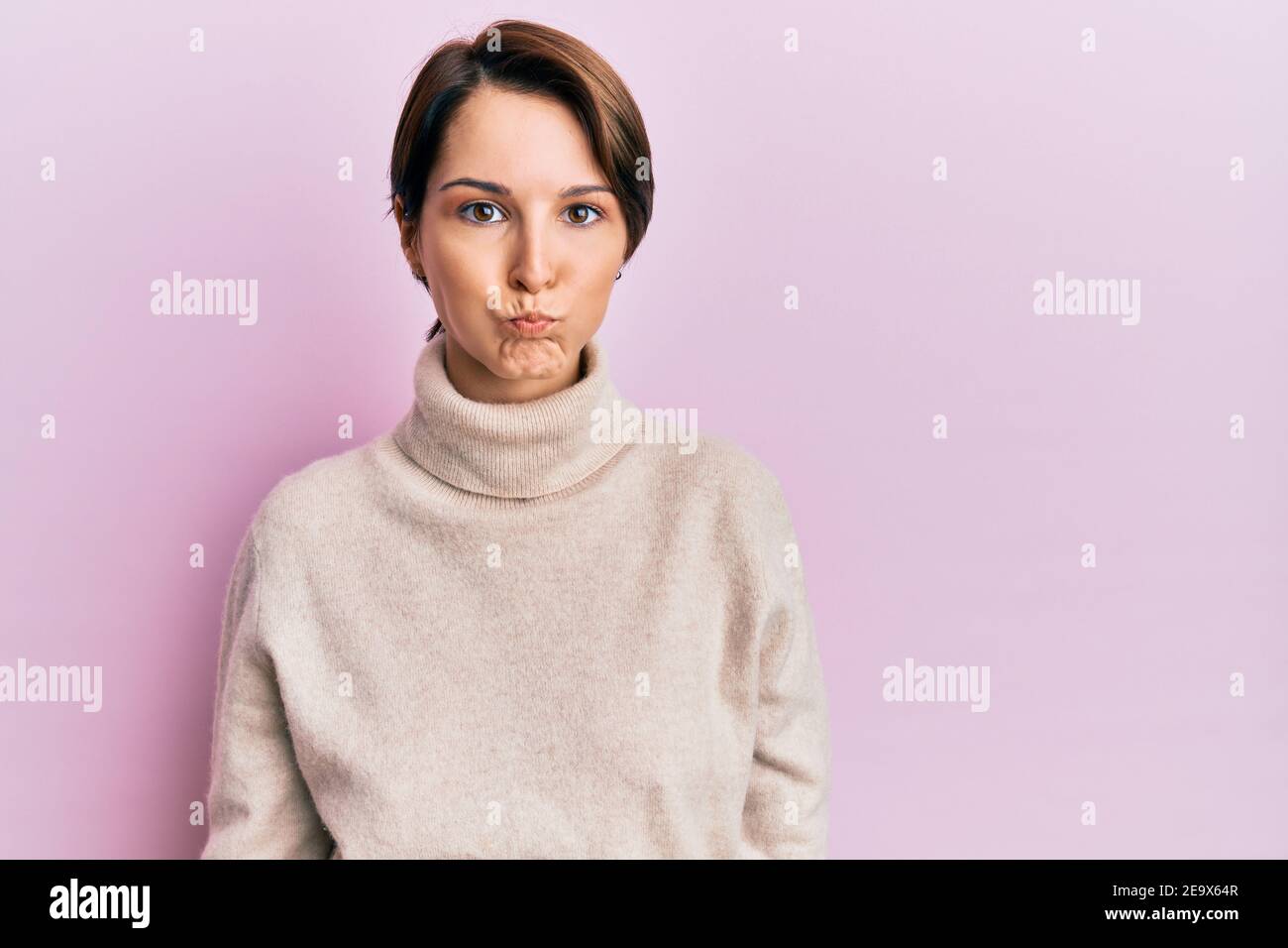 Puffing Cheeks Young brunette woman with short hair wearing casual winter sweater ...