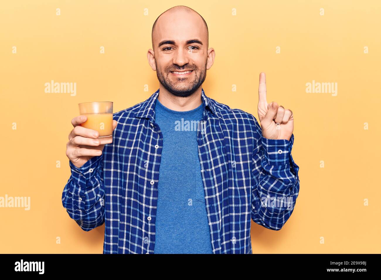 Young handsome bald man drinking glass of healthy orange juice smiling