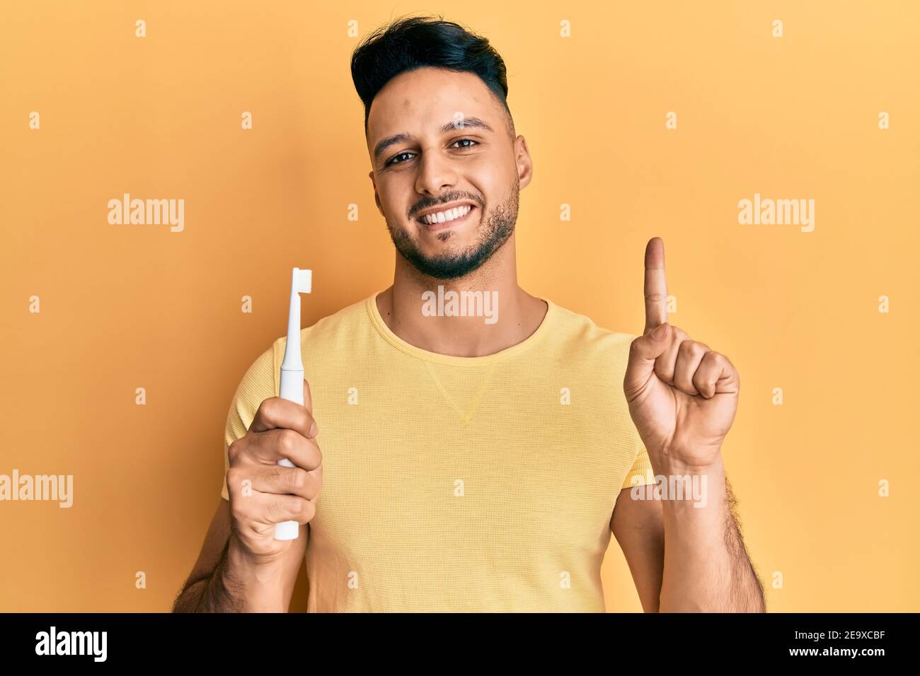 Young Arab Man Holding Electric Toothbrush Smiling With An Idea Or Question Pointing Finger With Happy Face Number One Stock Photo Alamy