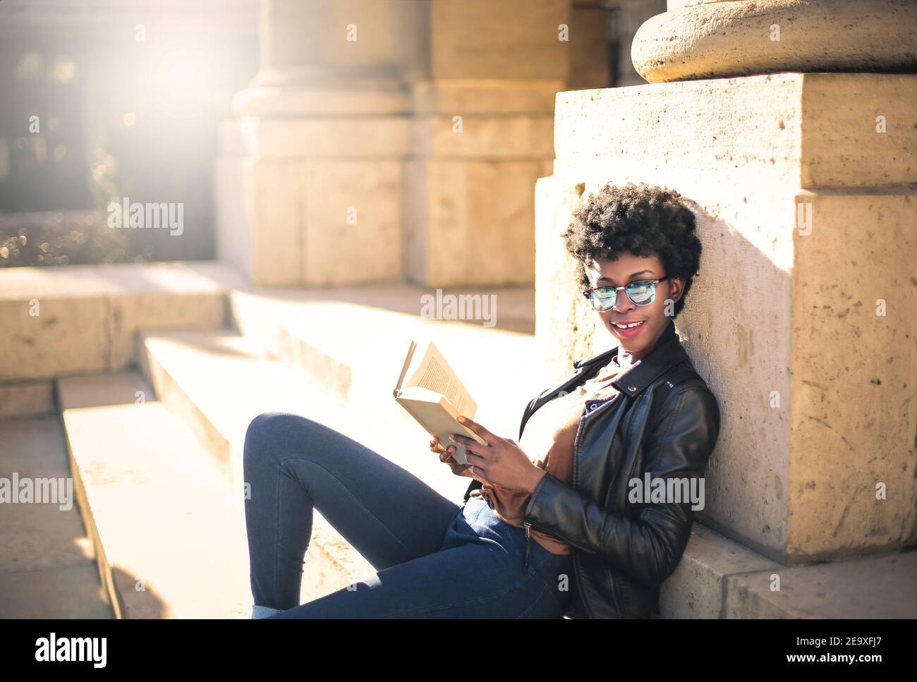 Shallow focus of an African woman with short curly hair reading a book in a park under the sunlight Stock Photo
