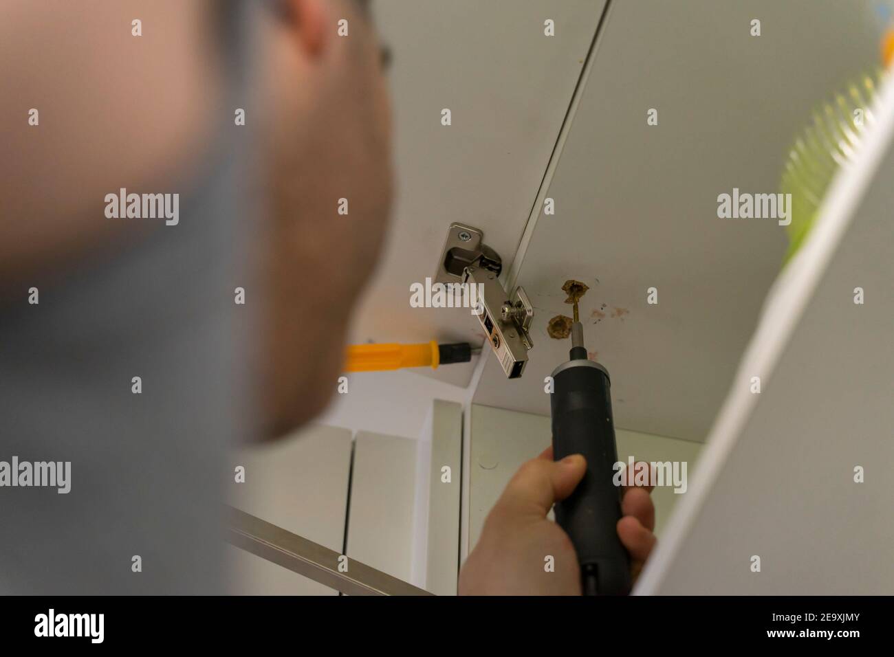 a worker fixing a kitchen cabinet with an electric screwdriver Stock Photo