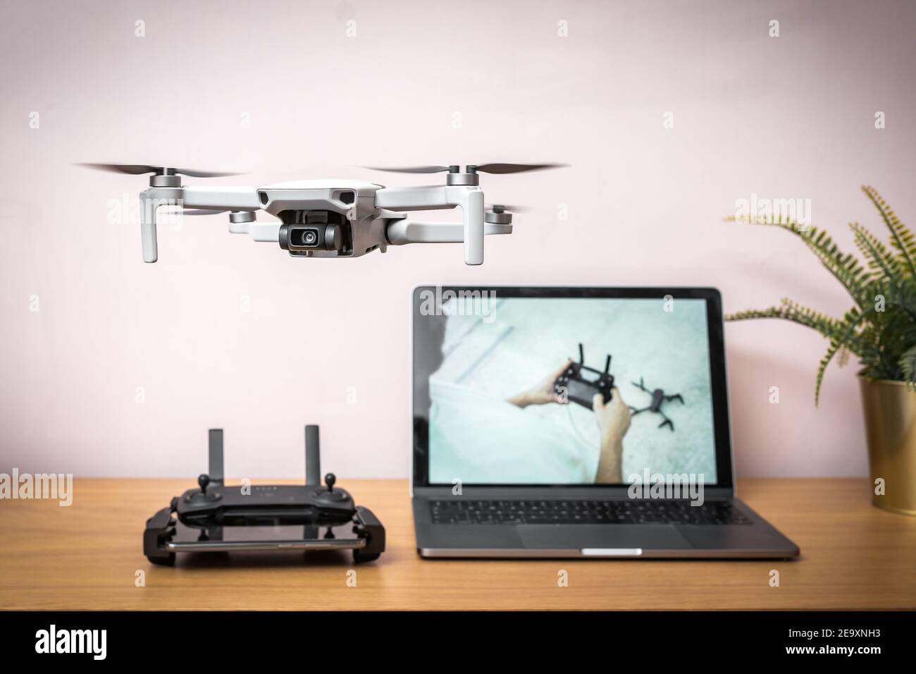 Learn how to fly drone flying in the air indoors safely with radio controller and laptop computer in the background showing online tutorial guide Stock Photo