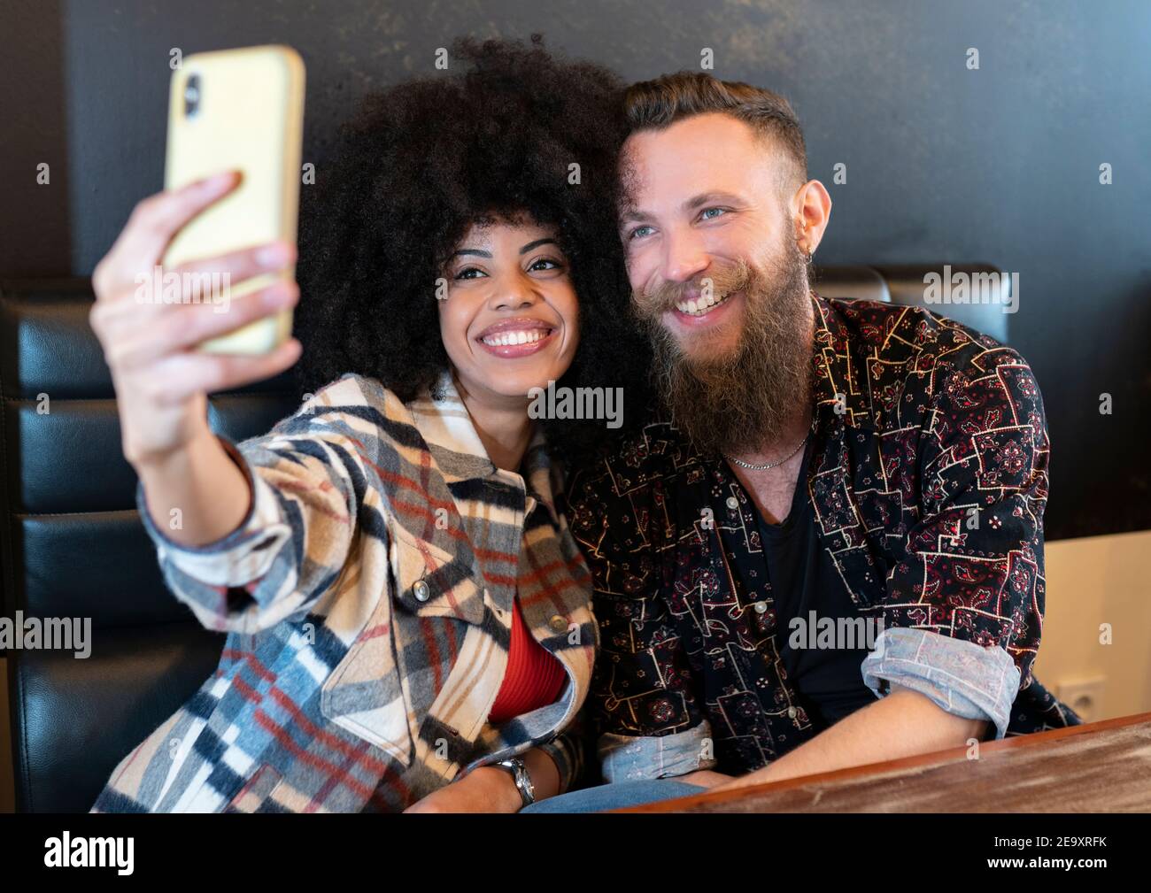 Delighted multiracial couple sitting at table in cafe and taking selfie on smartphone Stock Photo