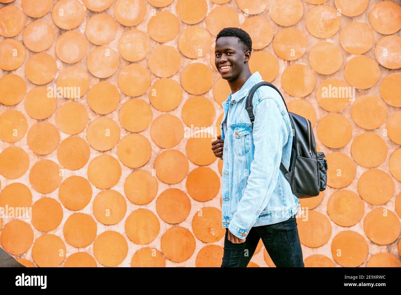 Young black man with denim jacket and backpack looking at the camera while walking Stock Photo
