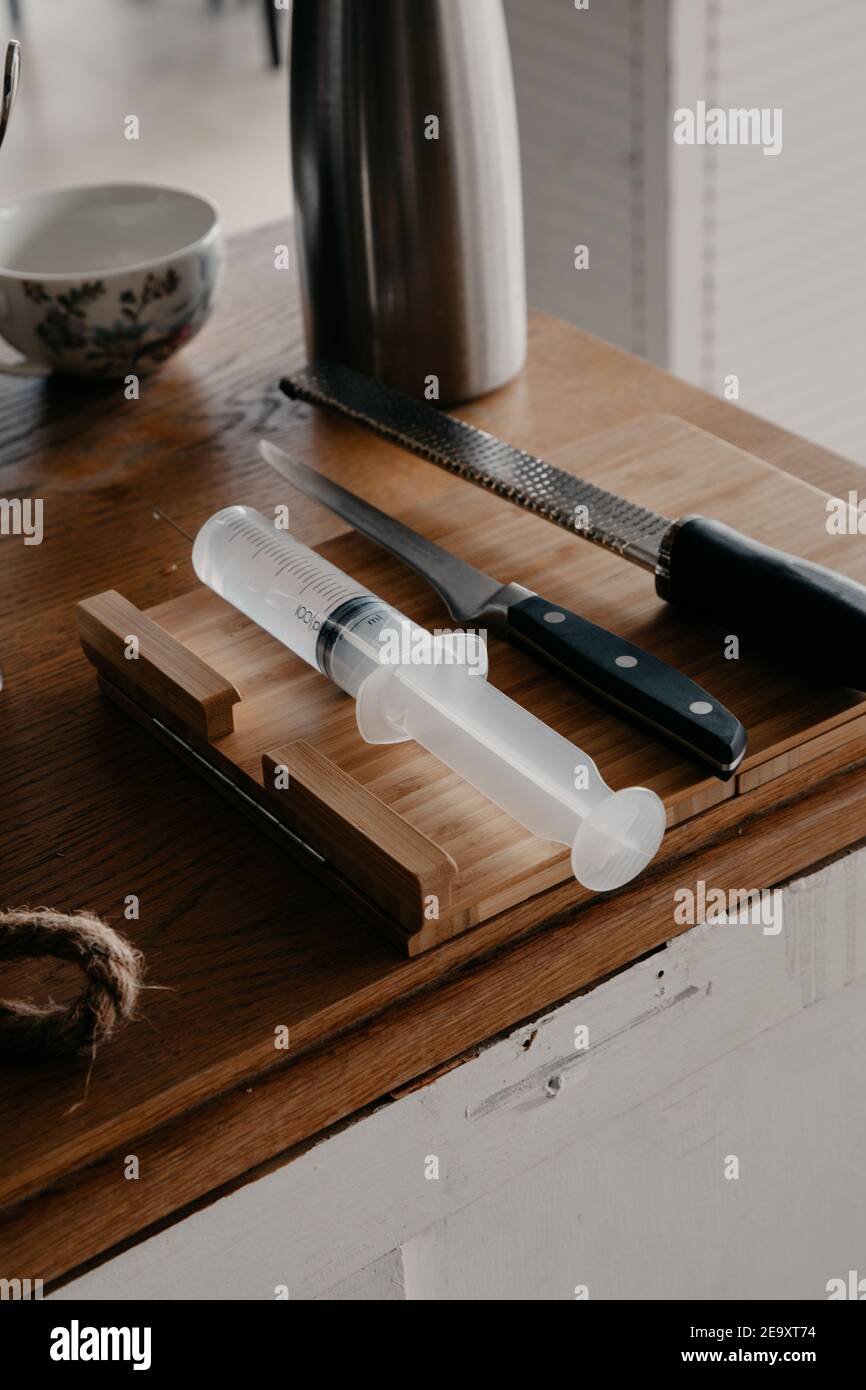 From above of various sharp knives and culinary syringe placed on wooden cutting board in kitchen Stock Photo
