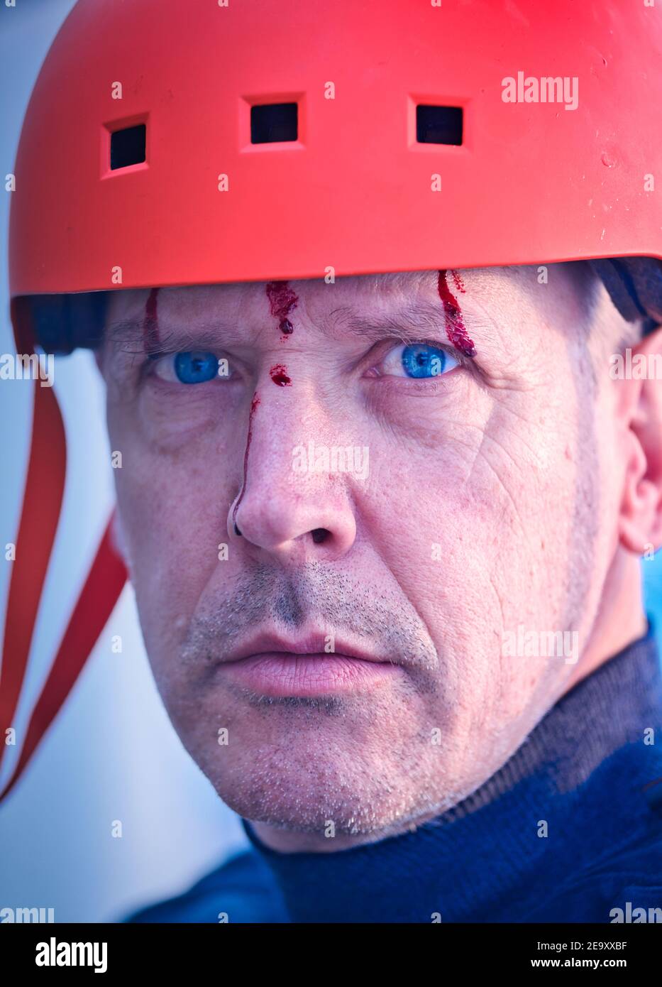 Serious middle aged man in orange cycling helmet with blood running down his face. Concept of intrigue, mystery curiosity, strange Stock Photo