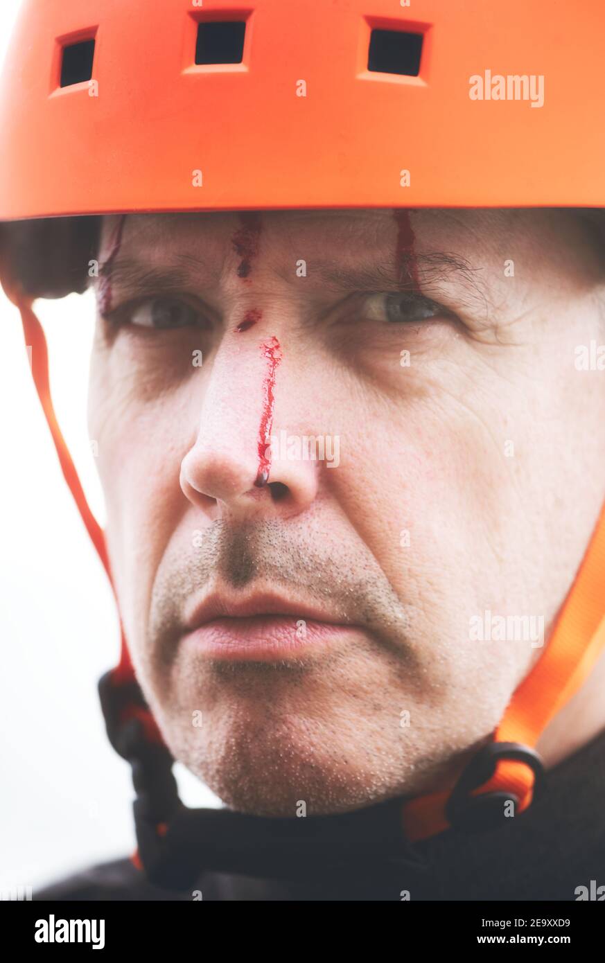 Serious middle aged man in orange cycling helmet with blood running down his face. Concept of intrigue, mystery curiosity, strange Stock Photo