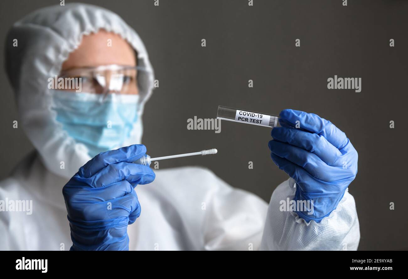 COVID-19 swab collection kit in doctor hands, nurse in personal protective equipment (PPE) suit holds tube of coronavirus PCR test. Concept of corona Stock Photo