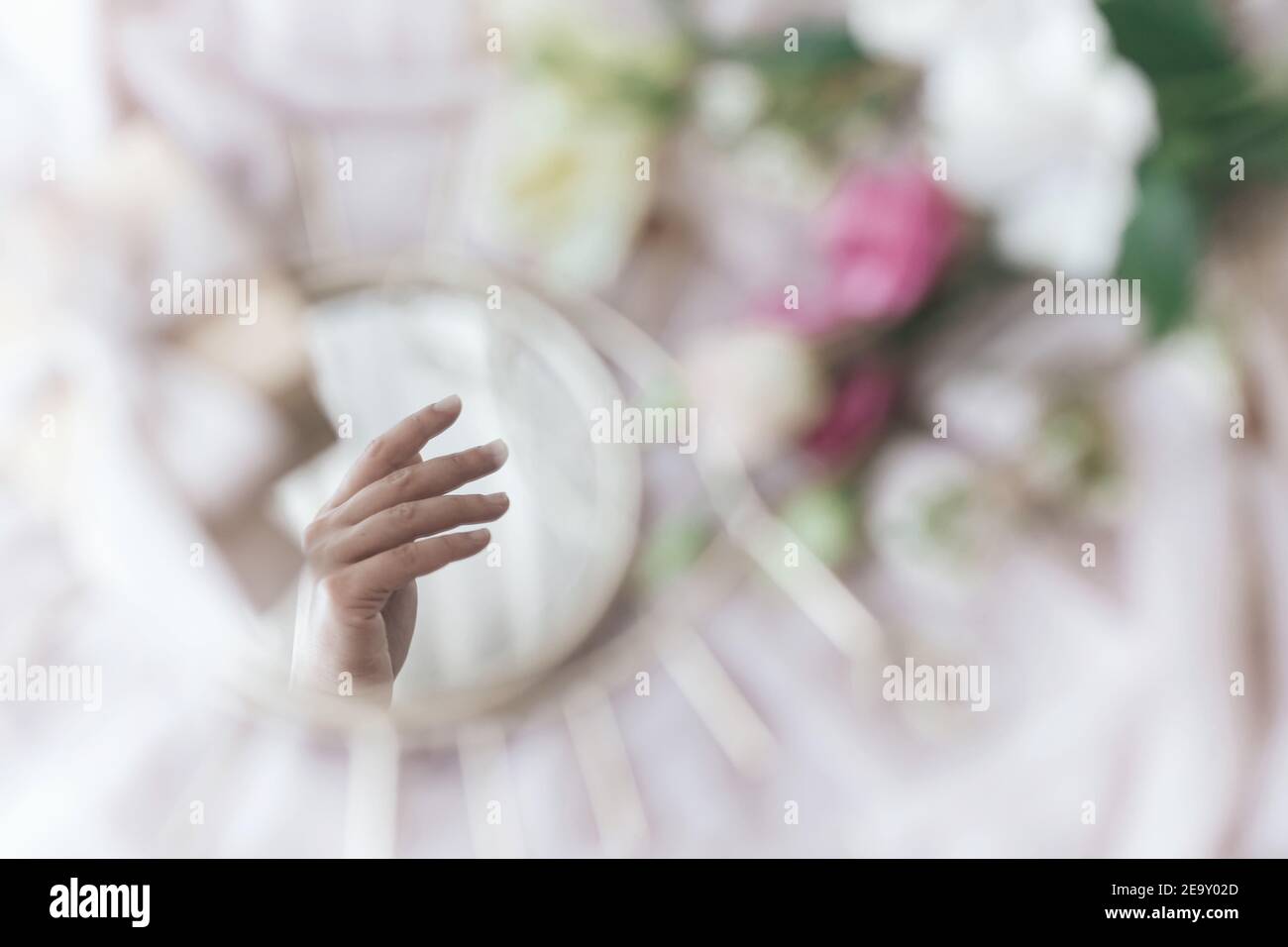 Hand reflected in mirror on background of soft fabric with flowers and gift box. Spring aesthetics. Gentle image. Eye shape boho mirror. Happy Womens Stock Photo