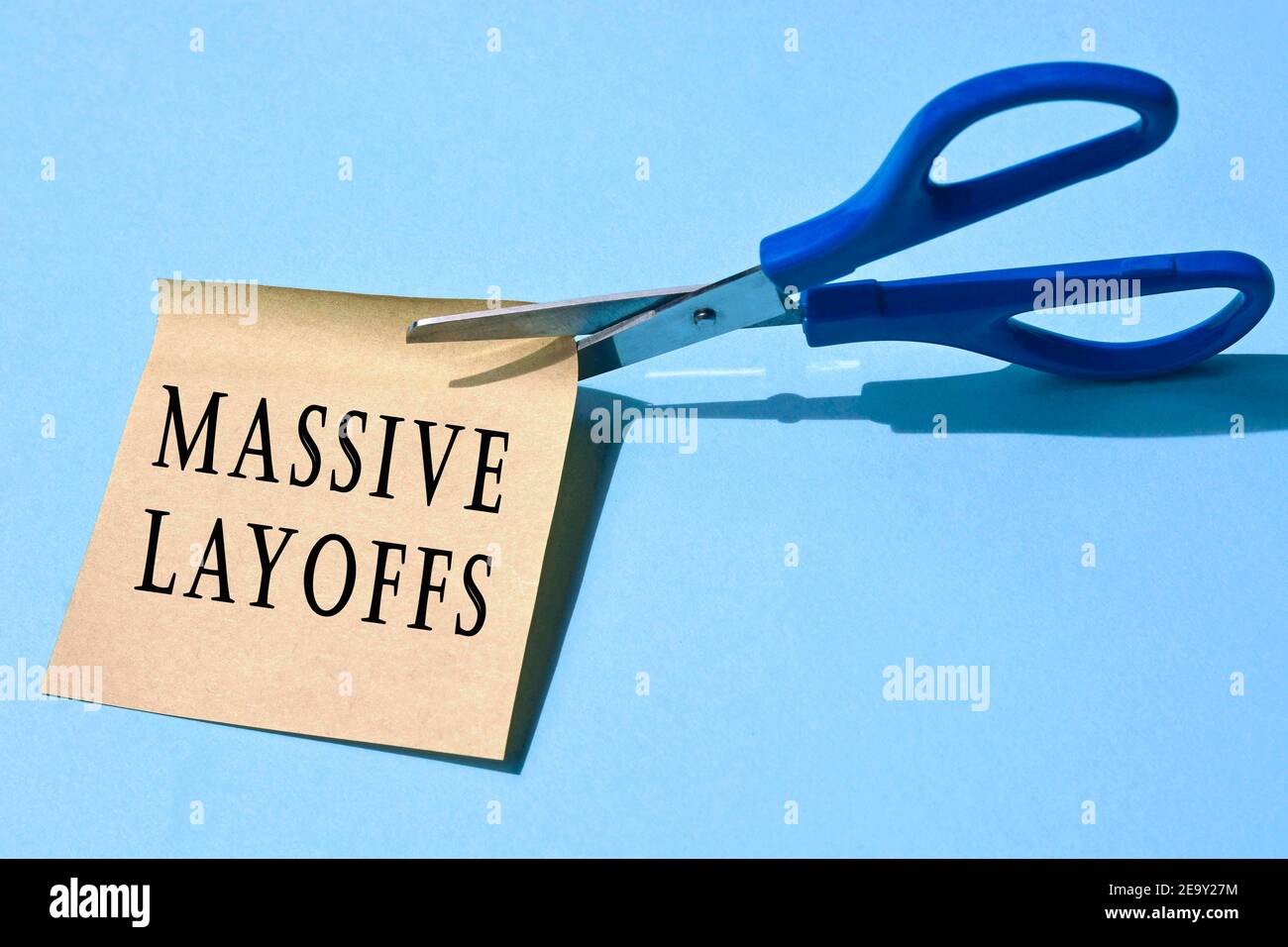 Scissors that cut yellow notepad with massive layoffs text on a blue background. Business concepts Stock Photo