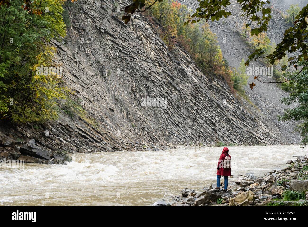 Woman in red coat standing on the banks of deep Prut river in Yaremche, Ukraine. Stock Photo