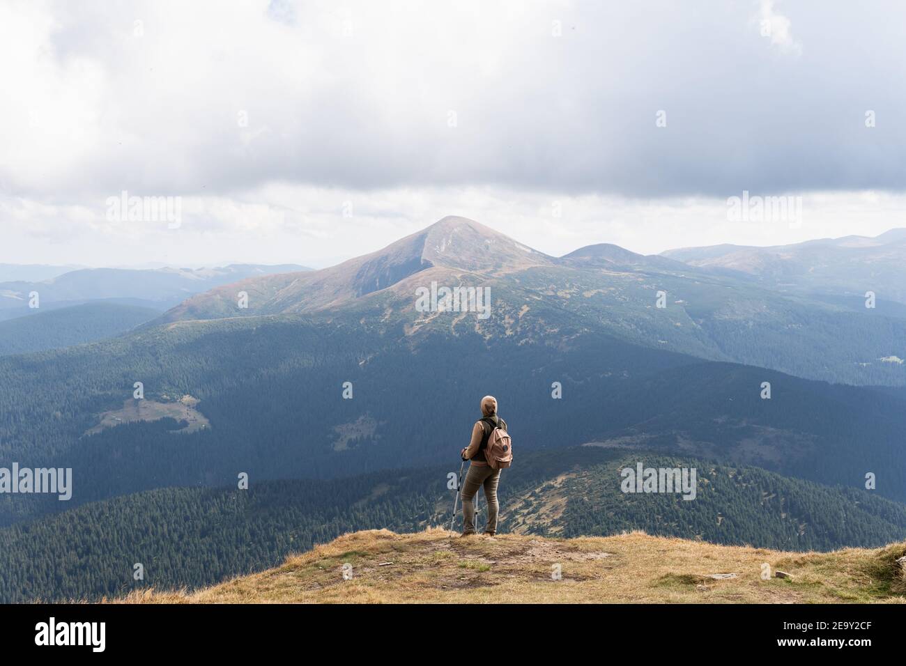 Woman hiking with backpack and trekking poles on summer day. Nature tourism in Ukrainian Carpathian mountains. Stock Photo