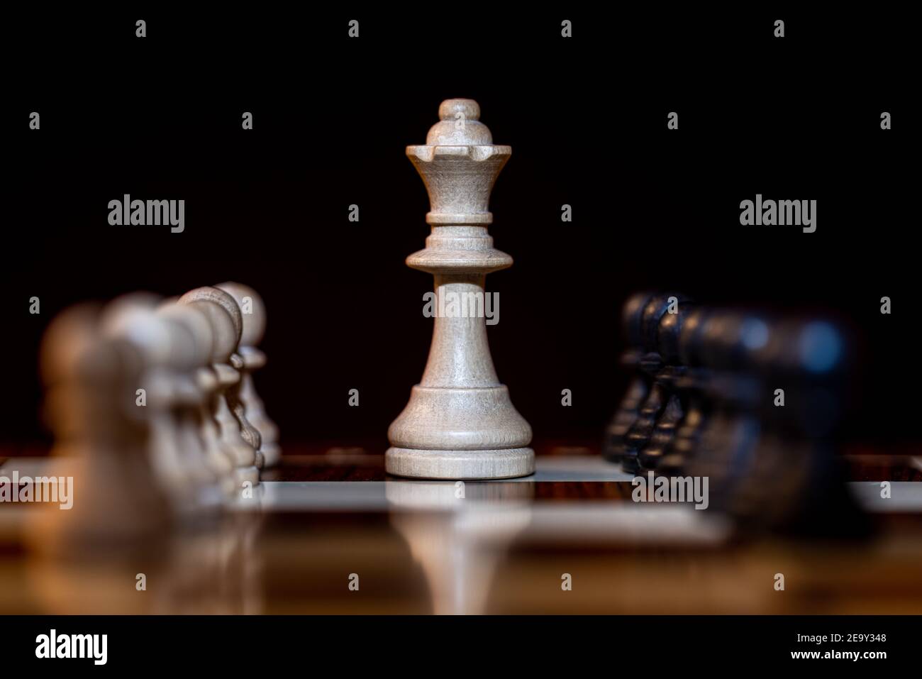 Chess White Queen on chessboard, surrounded by White and Black pawns against a black background- Single focus on the queen Stock Photo