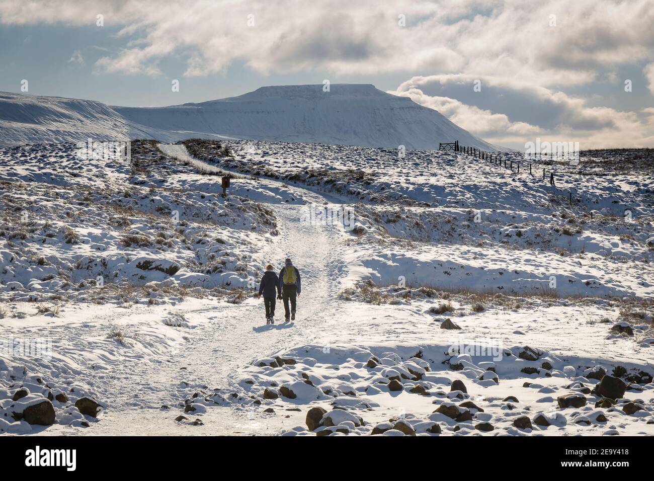 2 people walking in a snowy Yorkshire Dales landscape in winter. Taken at Blea Moor, Ribblehead, with a snow covered Ingleborough in the background Stock Photo
