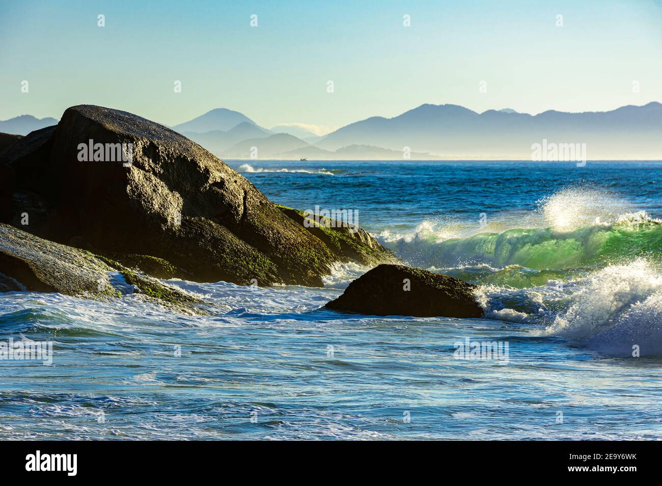 Waves crashing against the rocks at summer dawn on Devil beach in Ipanema Rio de Janeiro with mountains at background Stock Photo