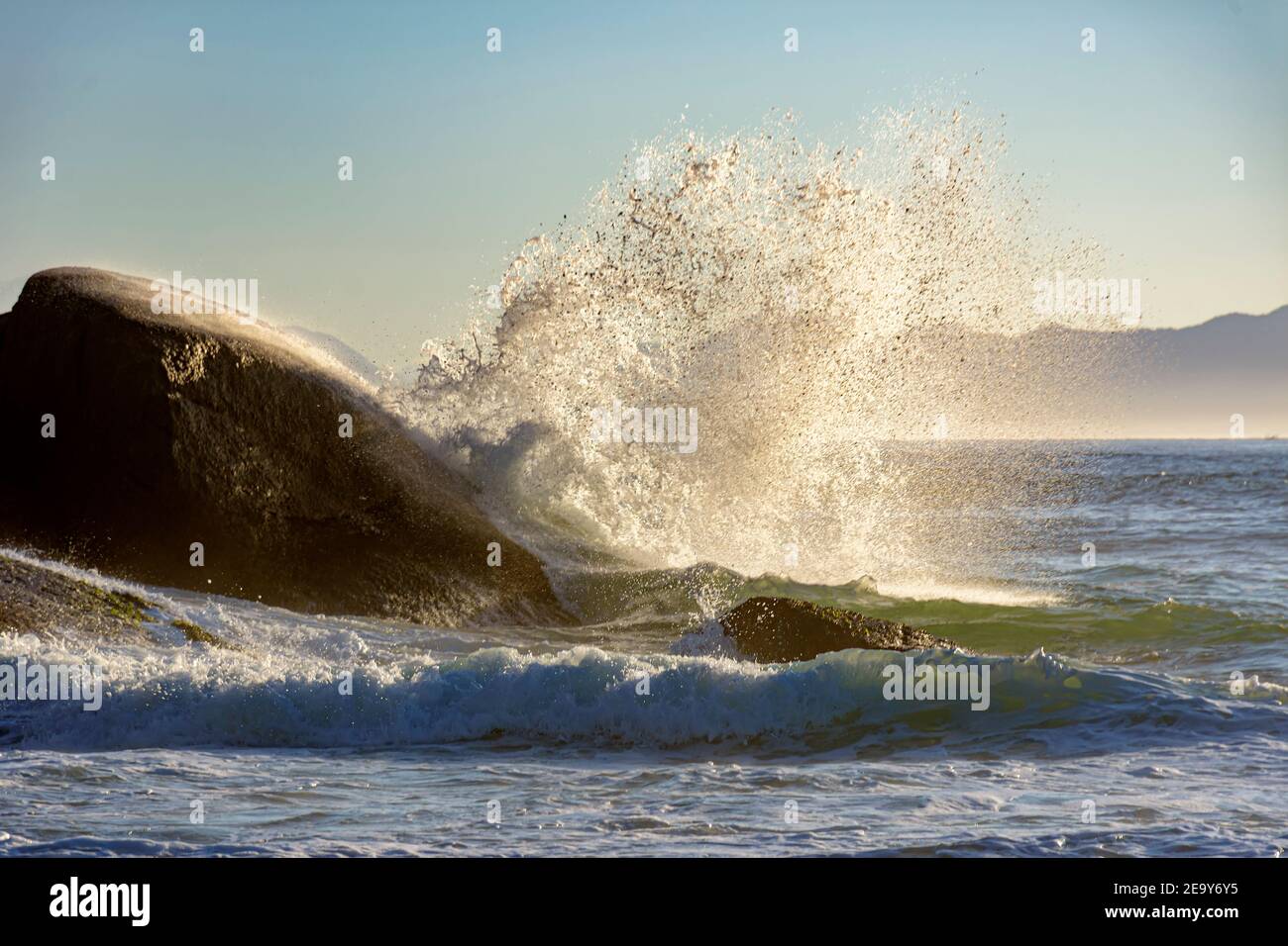 Waves crashing against the rocks at summer dawn on Devil beach in Ipanema Rio de Janeiro with mountains at background Stock Photo