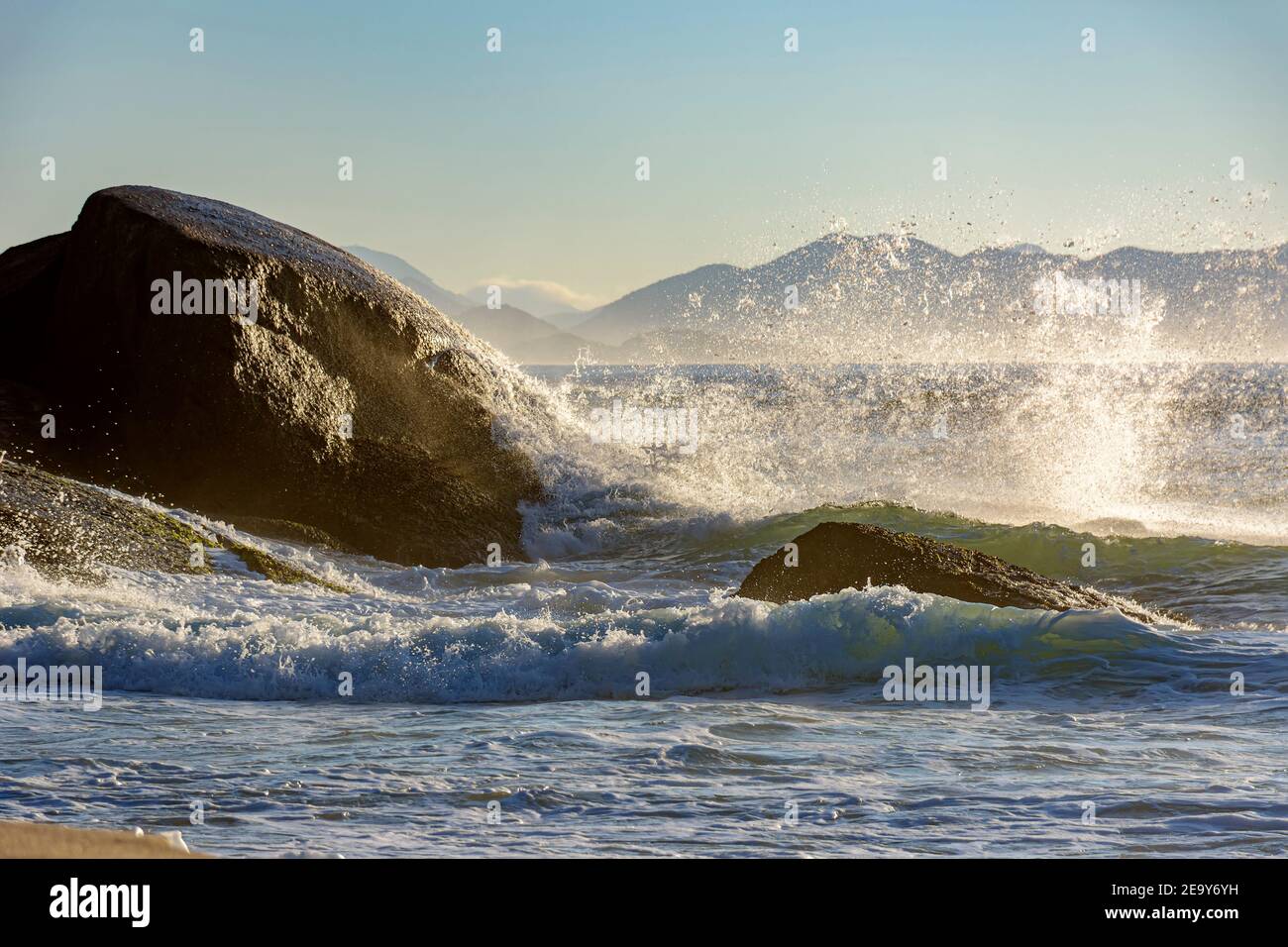 Waves crashing against the rocks at summer dawn on Devil beach in Ipanema Rio de Janeiro with mountains at background Stock Photo