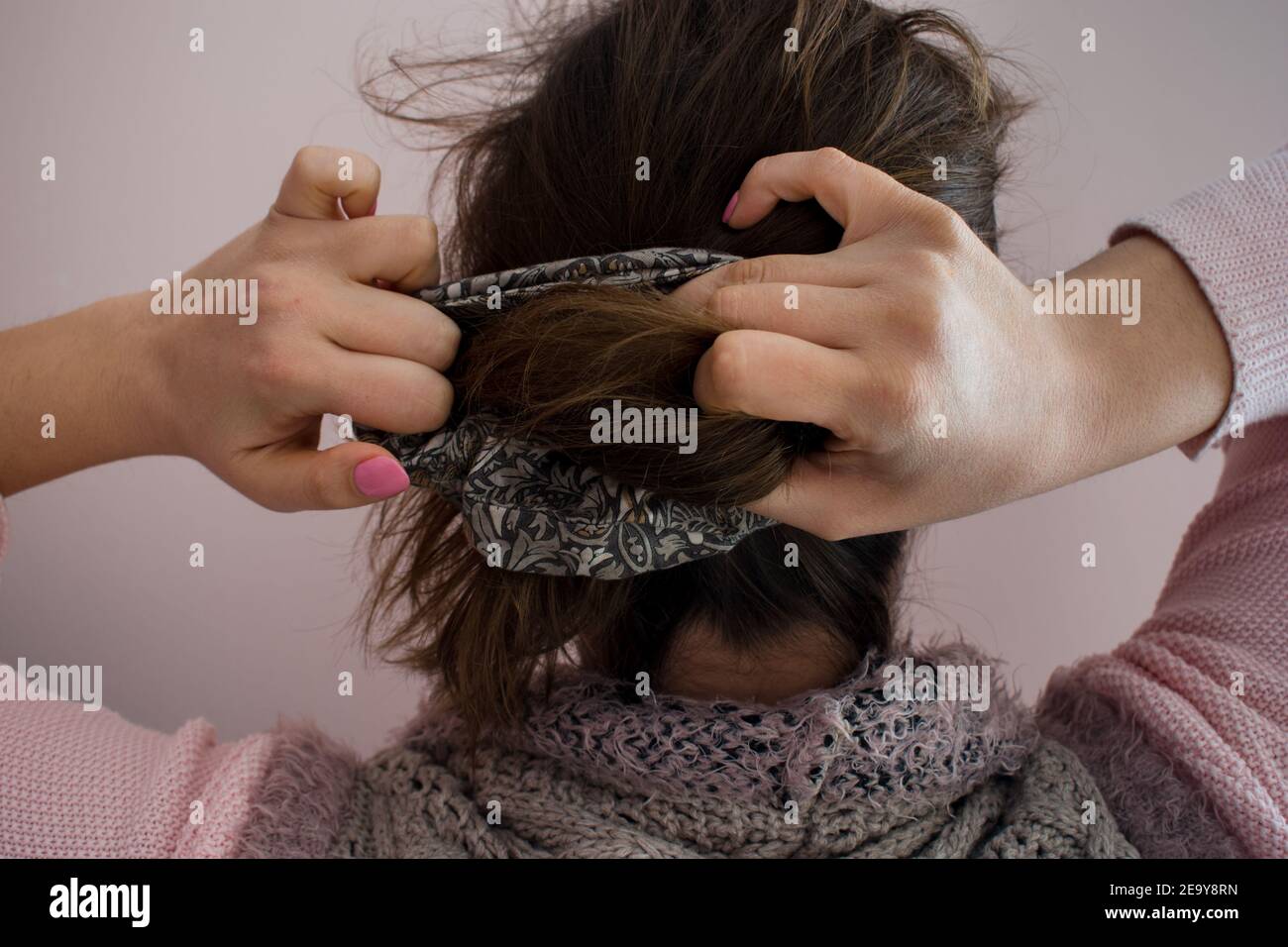 Young woman doing a ponytail with a scrunchie hair tie. View from the back. Stock Photo