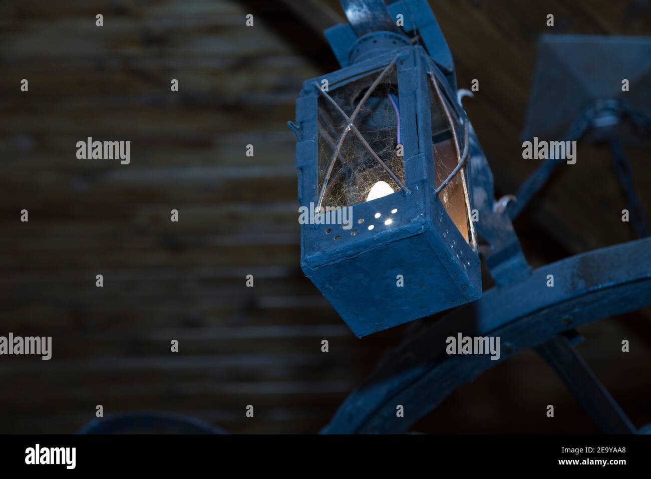 Blue old lamp in a cobweb is under seiling. Here is very dark background. Stock Photo