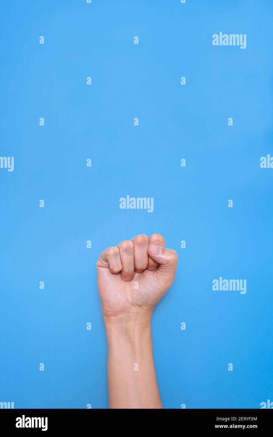 vertical shoot of the fist of an unrecognizable caucasian man with a blue background. concept of protest Stock Photo