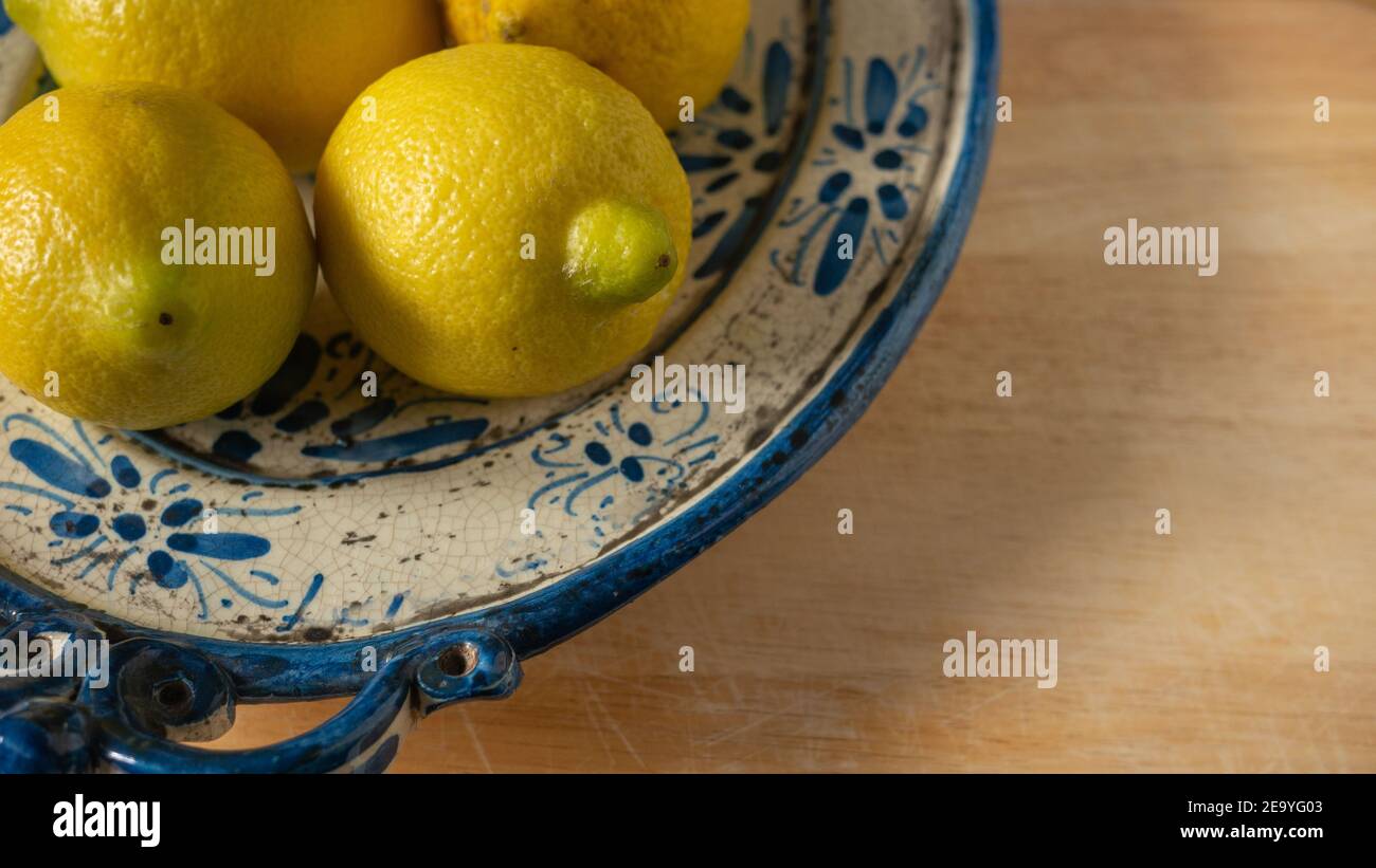 Fresh Mediterranean lemons on a beautiful blue and beige painted antique ceramic plate on a wooden table. Close up. Stock Photo