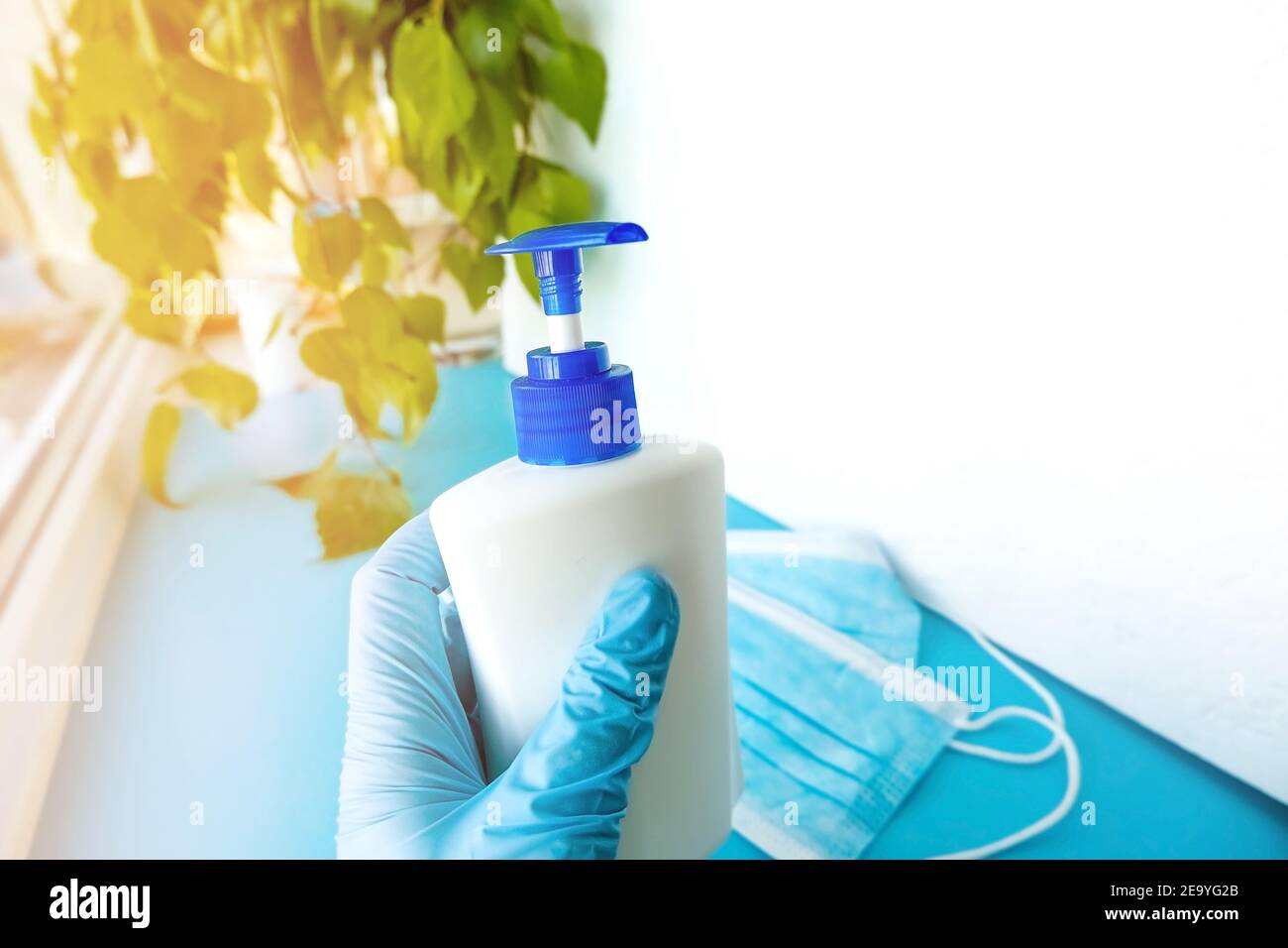 a hand in a medical glove holds a bottle with an antiseptic on a background of green sheets and a white background with masks, hygiene product, protec Stock Photo