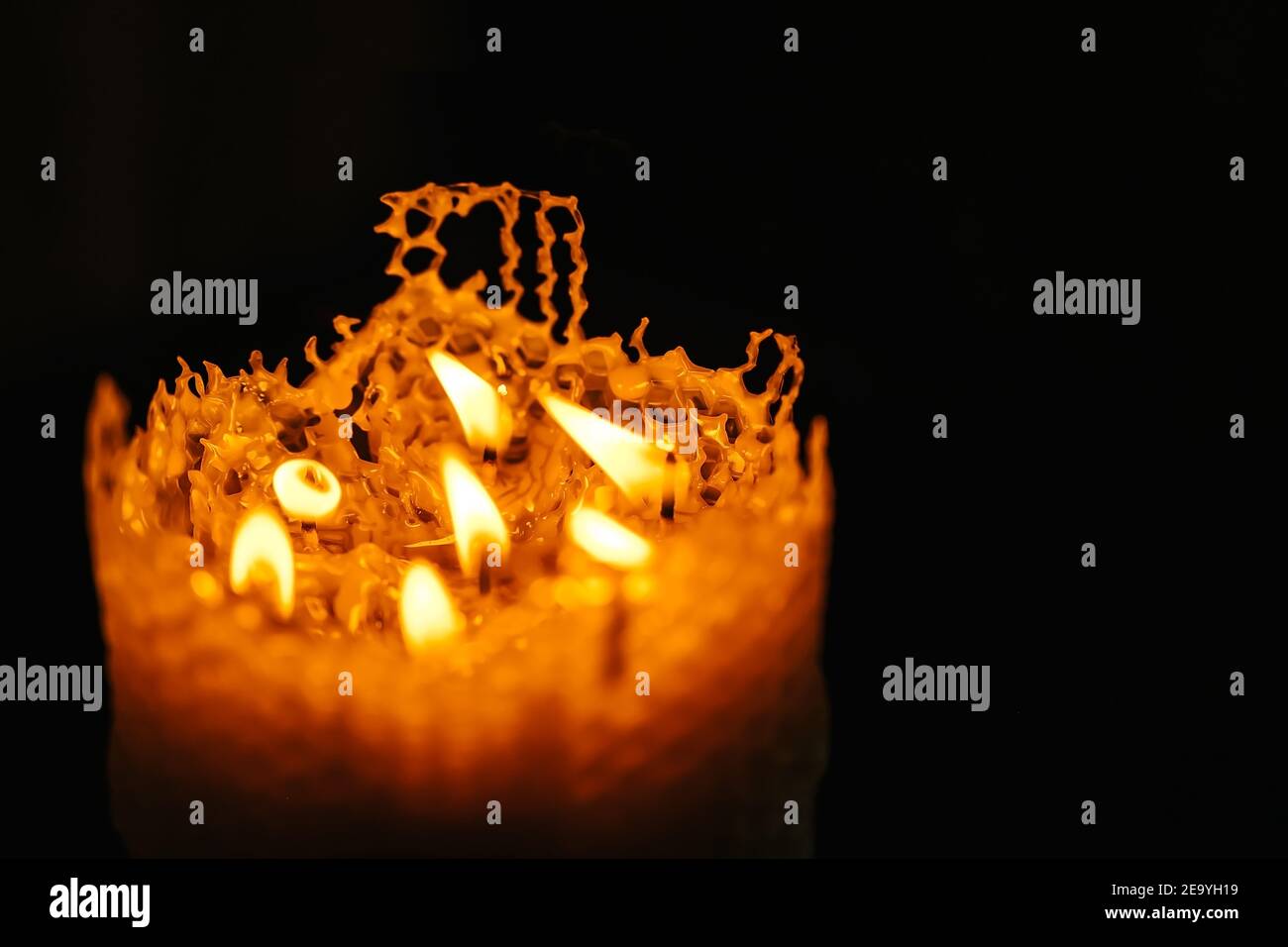 one large candle made of beeswax on a black background, seven small