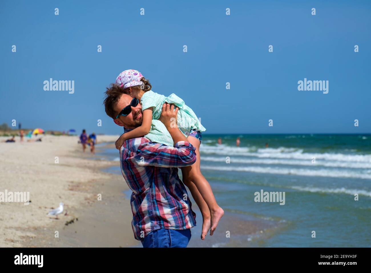 Happy dad picked up his little daughter. Young happy family walking along the seashore Stock Photo