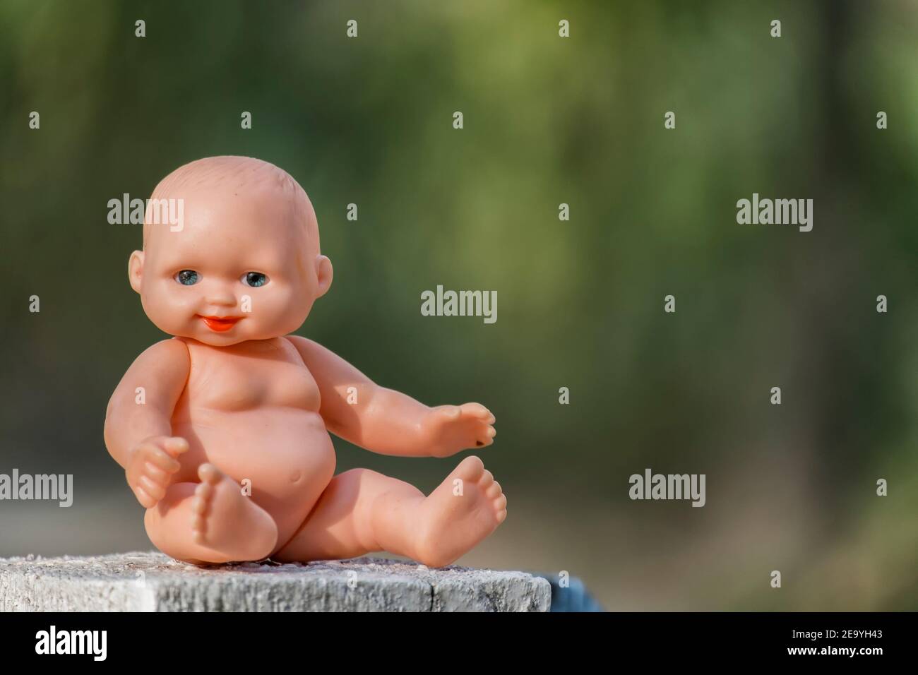 Old little naked baby doll on a blurry green background Stock Photo