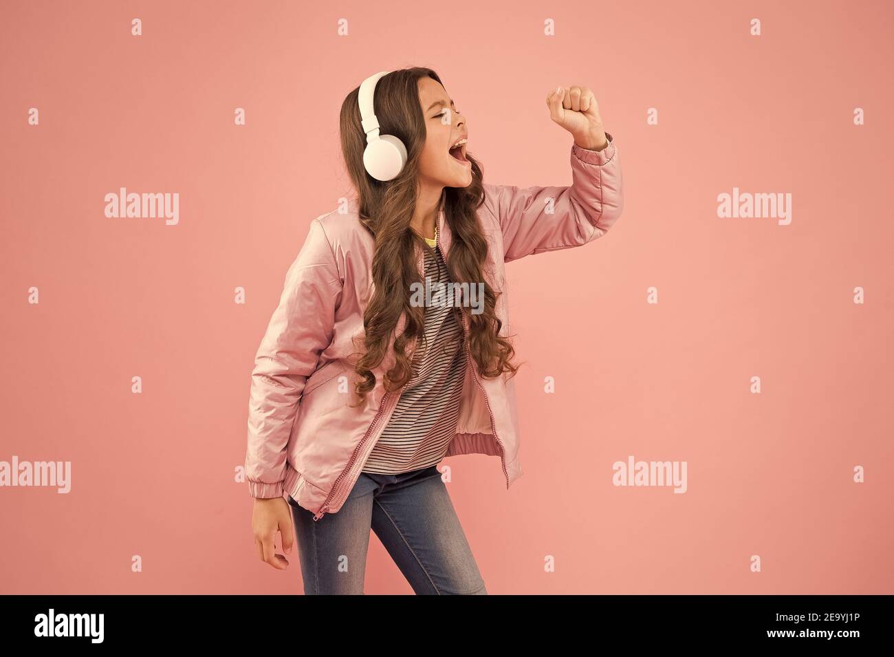 Imagine she is a star. Karaoke party fun. Fun and entertainment. Joining in a song. Small girl with sad look pink background. Little child hear stereo sound. Enjoying song playing in headphones. Stock Photo