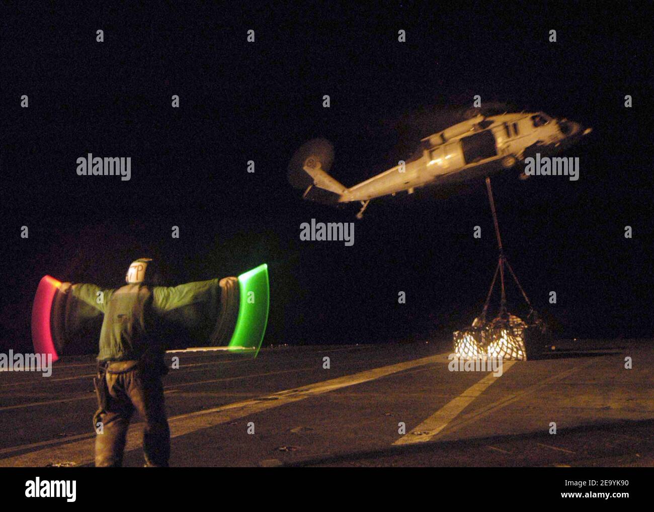 Aviation Machinist's Mate Airman Carlos Martinez of Silver Spring, Md., uses lighted wands to direct an MH-60S Knighthawk helicopter, assigned to the 'Gunbearers' of Helicopter Combat Support Squadron Eleven (HC-11), to drop a cargo net full of relief supplies on the flight deck aboard USS Abraham Lincoln (CVN 72) during a night vertical replenishment with a nearby supply ship. Helicopters assigned to Carrier Air Wing Two (CVW-2) and Sailors from Abraham Lincoln are supporting Operation Unified Assistance, the humanitarian operation effort in the wake of the Tsunami that struck South East Asia Stock Photo