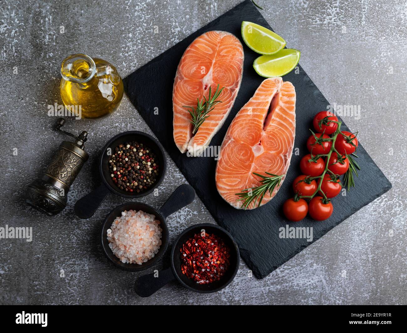 two raw fresh steak fish trout, salmon and spices on black stone surface Stock Photo