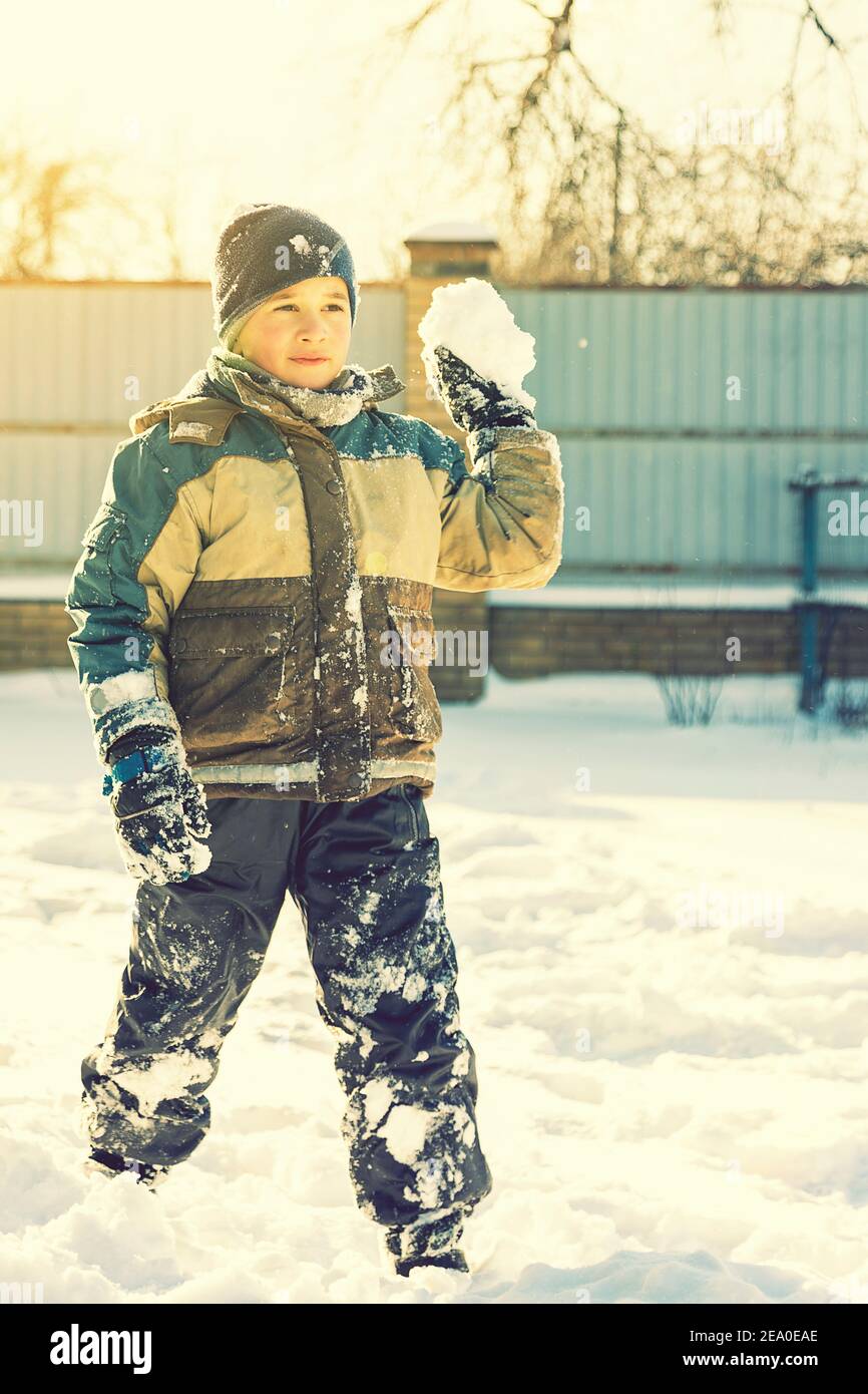 Baby boy walking at snowfall. Child in winter clothes playing with snow. boy making snowball outdoor. Boy playing snowballs in winter park. Christmas Stock Photo