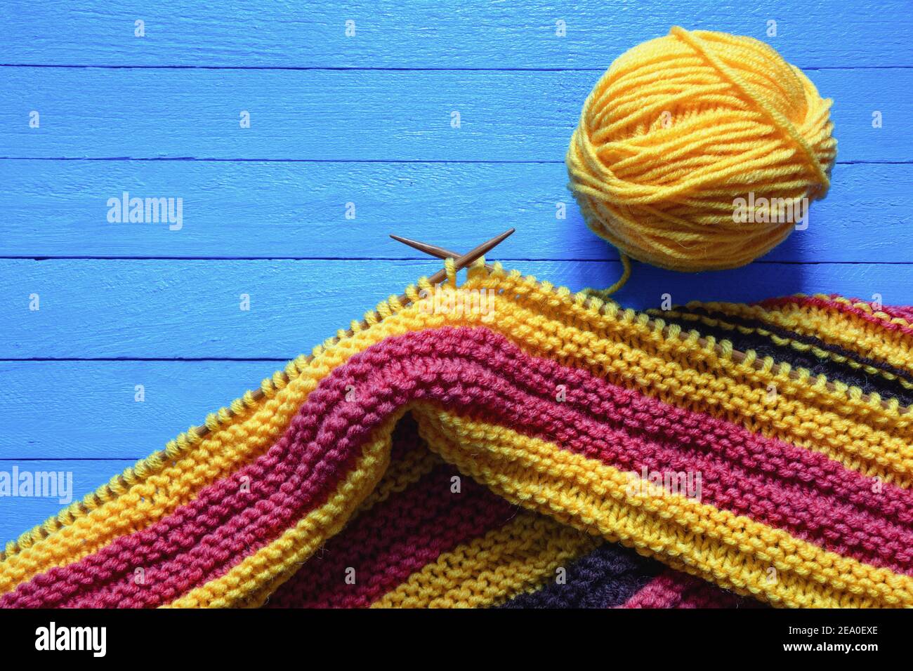 Hobbies concept. Bright striped knitted cloth with knitting needles and