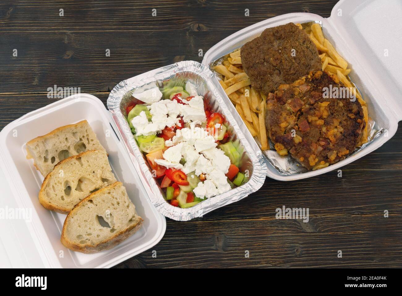 Food delivery. Bread, salad and pljeskavica - grilled dish of minced meat,  french fries in takeaway containers on rustic wooden table Stock Photo