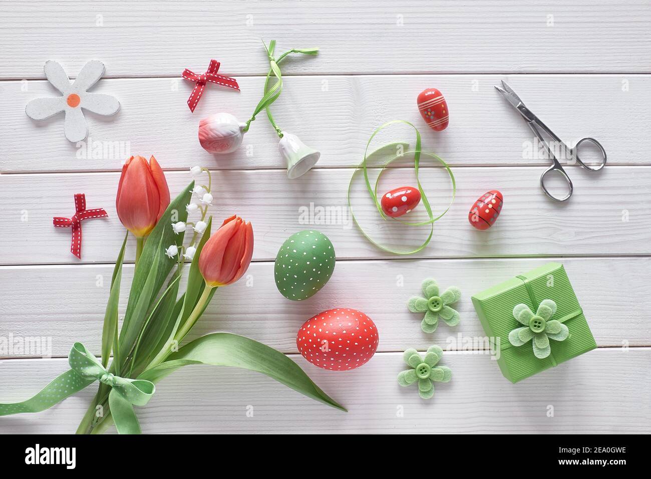 Flat lay with red tulips in rattan wreath basket and green grass. Decorative painted Easter eggs. Springtime, Easter background on rustic off white wo Stock Photo