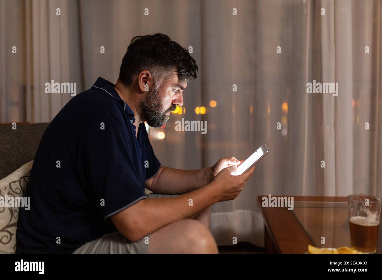 bearded man on sofa uses digital tablet in dining room overnight Stock Photo