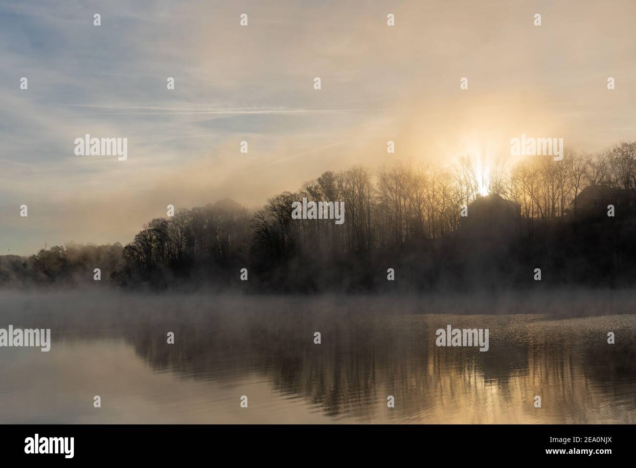 The sun rises behind a house on Lake Lanier in Georgia with fog rising on the surface of the water under a blue and orange sky; landscape view Stock Photo