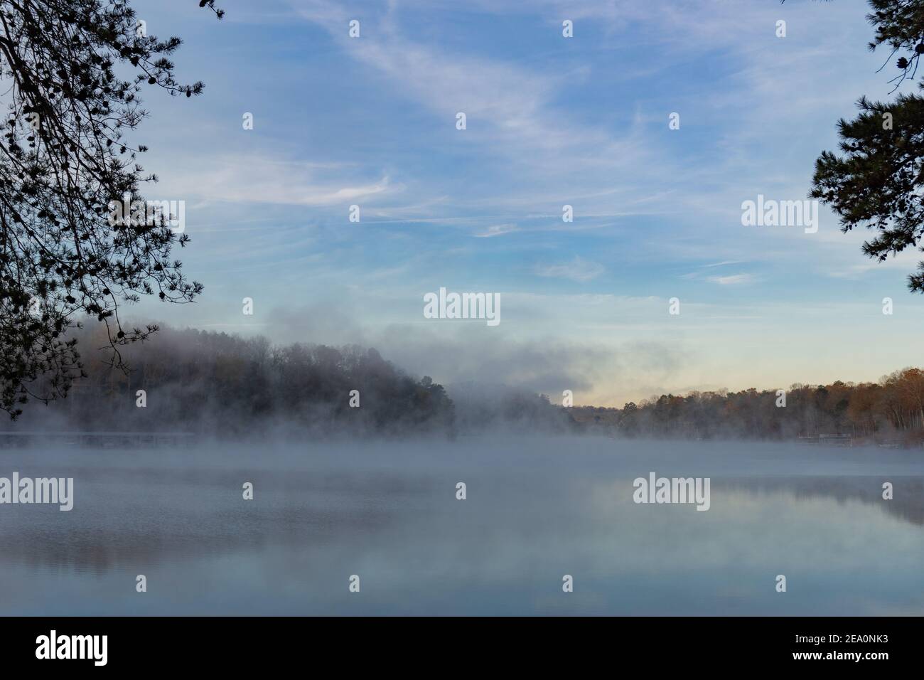 A wall of fog rises on the surface of the water of Lake Lanier in Georgia at dawn in winter framed by trees; landscape view Stock Photo