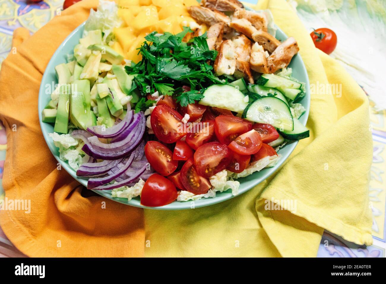 Chicken paleo diet salad nutrition with meat, yelloe mango, avocado and fresh vegetables ingredients in bowl on colorful background Stock Photo