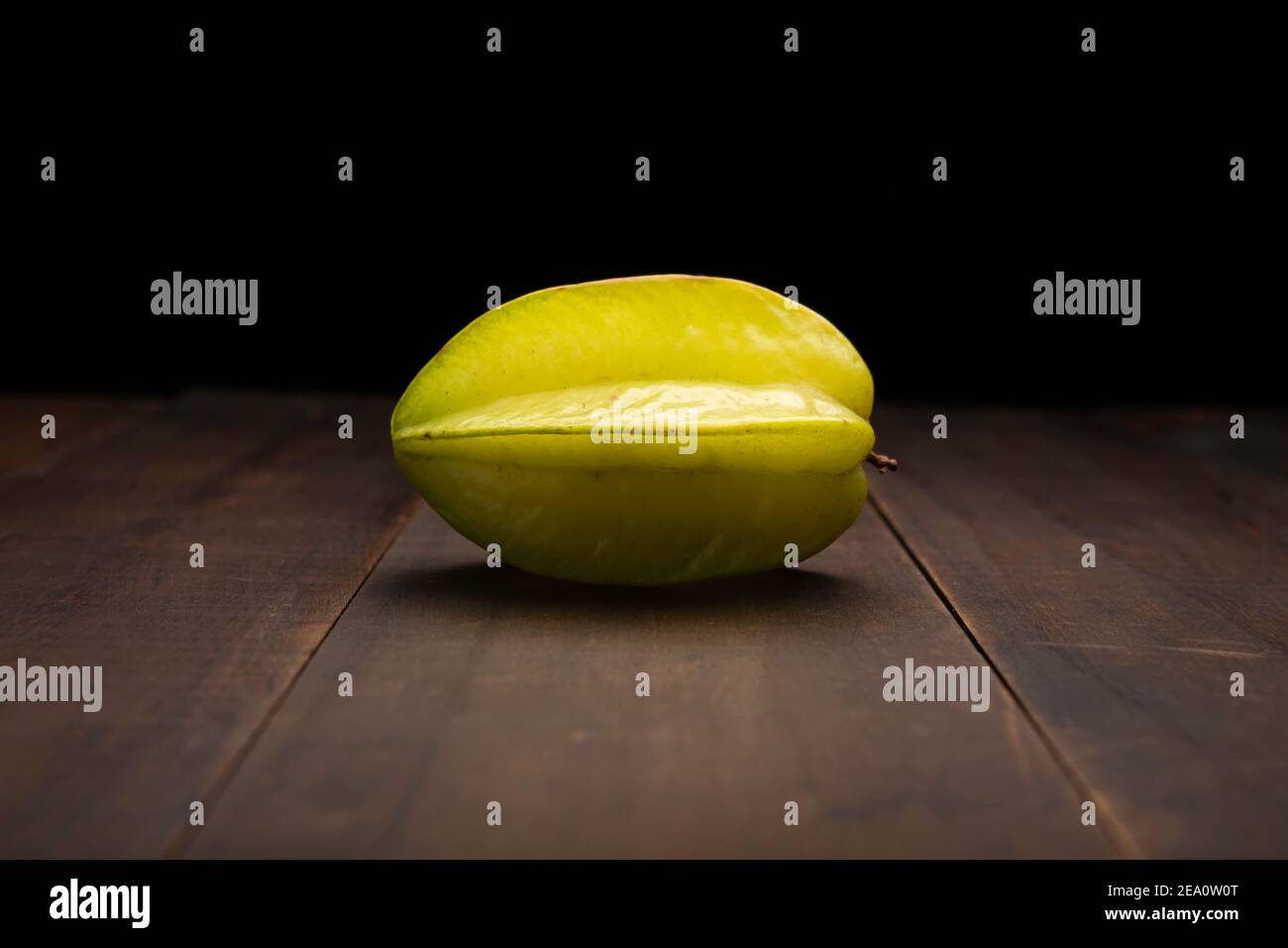 still life image of one starfruit or carambola. Close up on rustic wooden surface and black background Stock Photo