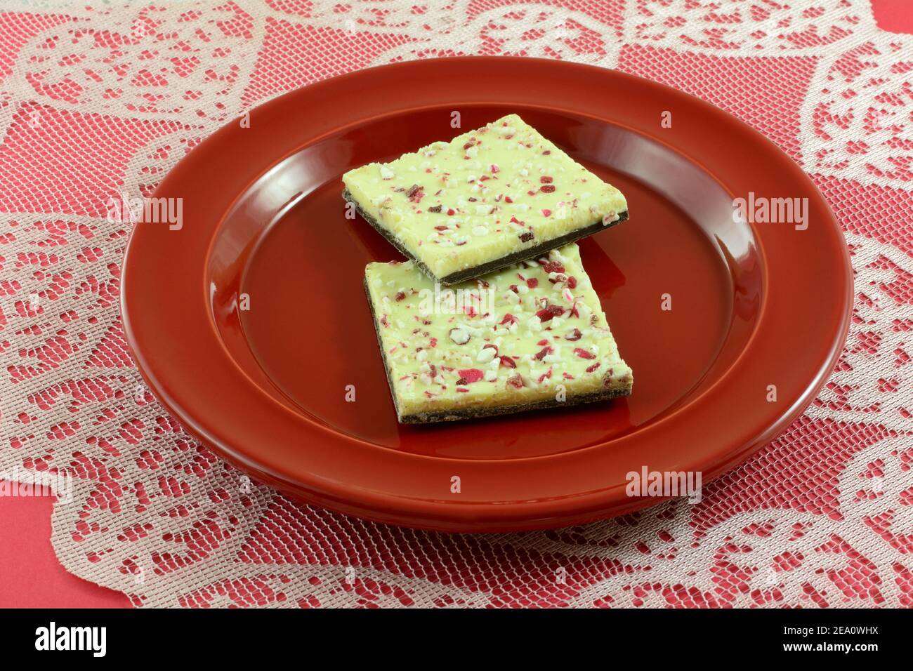 White chocolate peppermint bark on top of dark chococlate candy on red plate on heart lace tablecloth runner Stock Photo